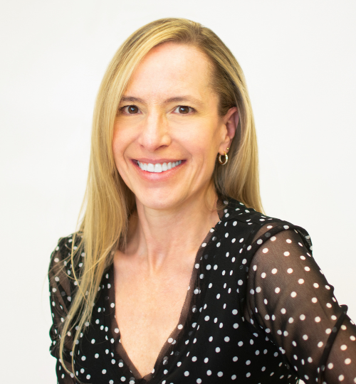 Gretchen Clutter, blonde woman smiling for the camera and wearing a black v-neck blouse with white polka dots.