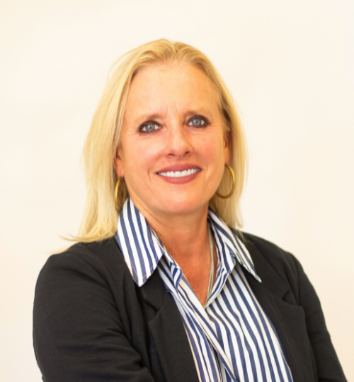 Stacey Ellis, a middle-aged blonde woman smiling for the camera, wearing a blue and white vertical striped Oxford button down with a black blazer over top and hoop earrings.